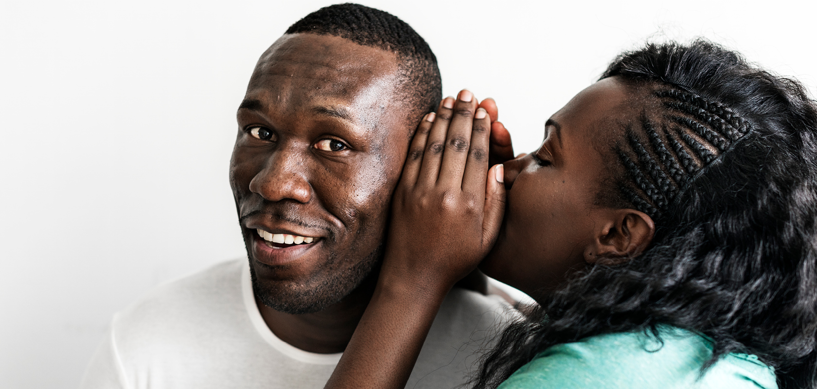 African American woman whispering into smiling African American man's ear