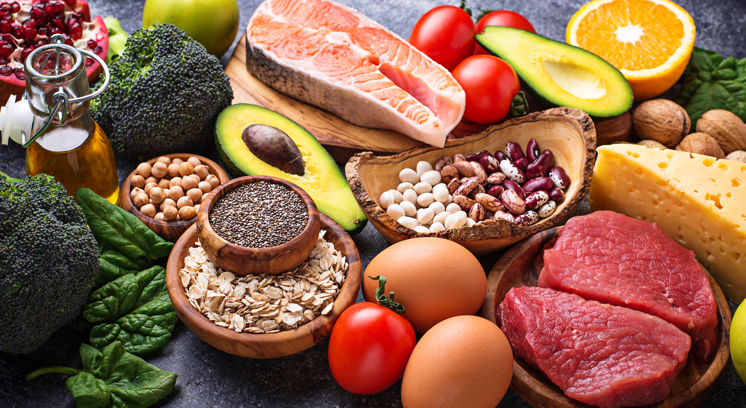 Colorful mix of healthy foods including broccoli, grains, nuts, avocado, tomato,salmon, red meat, fruit