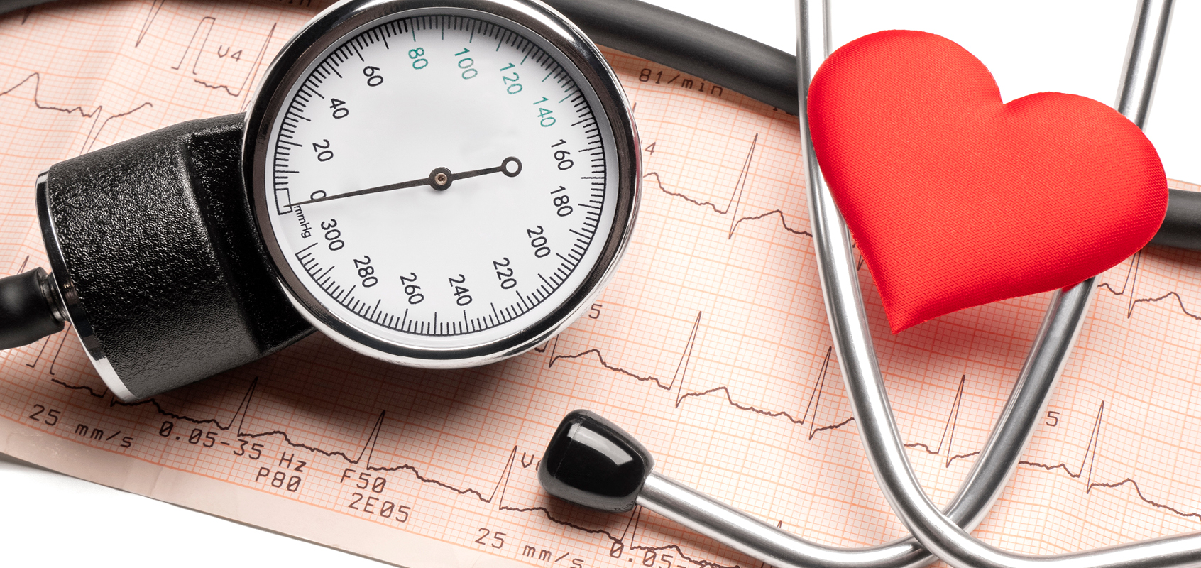 Close-up of blood pressure dial with stethoscope and red heart figurine on top of blood pressure readout paper