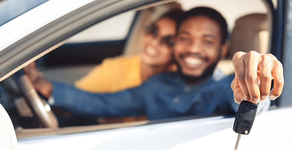Smiling African-American couple holding key to car outside window preparing to donate car to charity